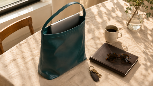 Interior shot of a leather crafting workshop featuring racks of leather hides and a finished burgundy shoulder bag resting on a wooden bench.